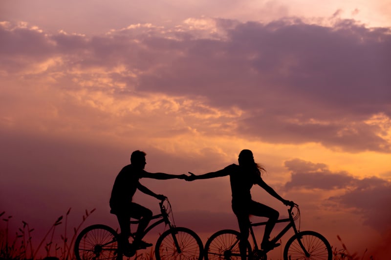 Two cyclists riding side by side at sunset, hands joined