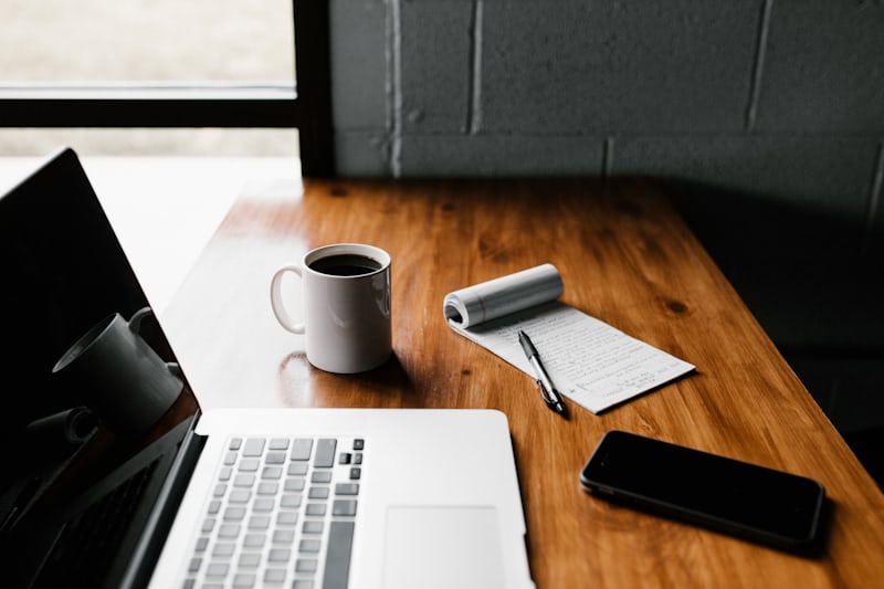 A laptop, a notebook and a cup of coffee on a wooden desk